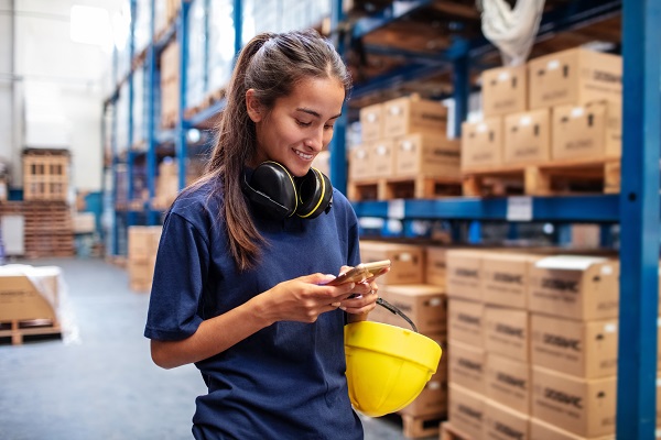Young woman using her mobile phone in large warehouse.