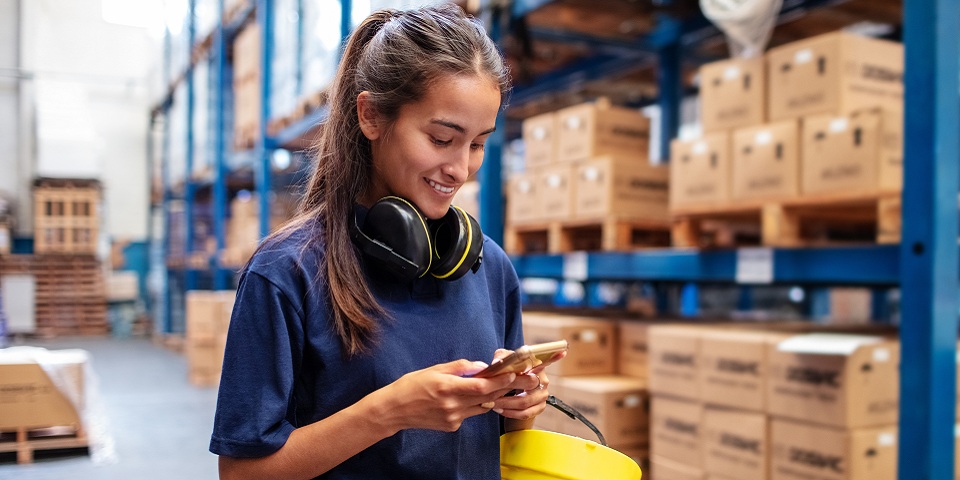 Young woman using her mobile phone in large warehouse.