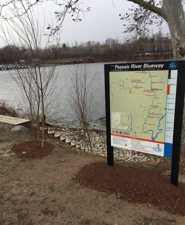 A Passaic River Blueway canoe and kayak trail sign beside the river in New Jersey.