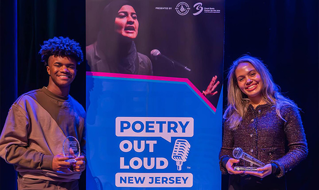 teenagers hold trophies next to event banner